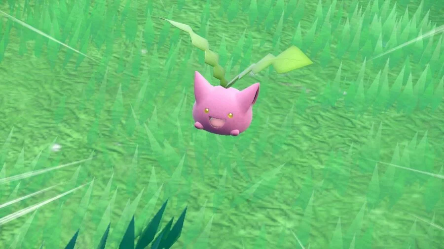 Hoppip, a round pink Pokémon with large ears and two green shoots growing from its head, against a grassy field.