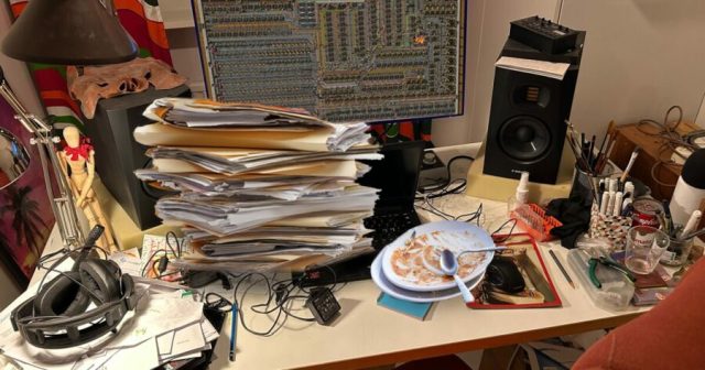 Man Can Hardly See Perfectly Organized Factorio Base Over Gigantic Pile of Shit on Desk